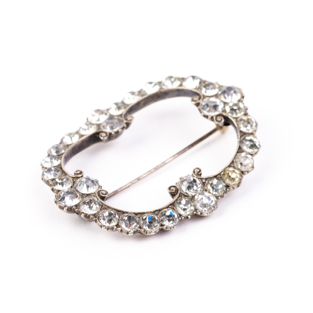 A nineteenth-century Victorian openwork oval buckle brooch set with faceted clear paste glass stones in a silver setting. View V