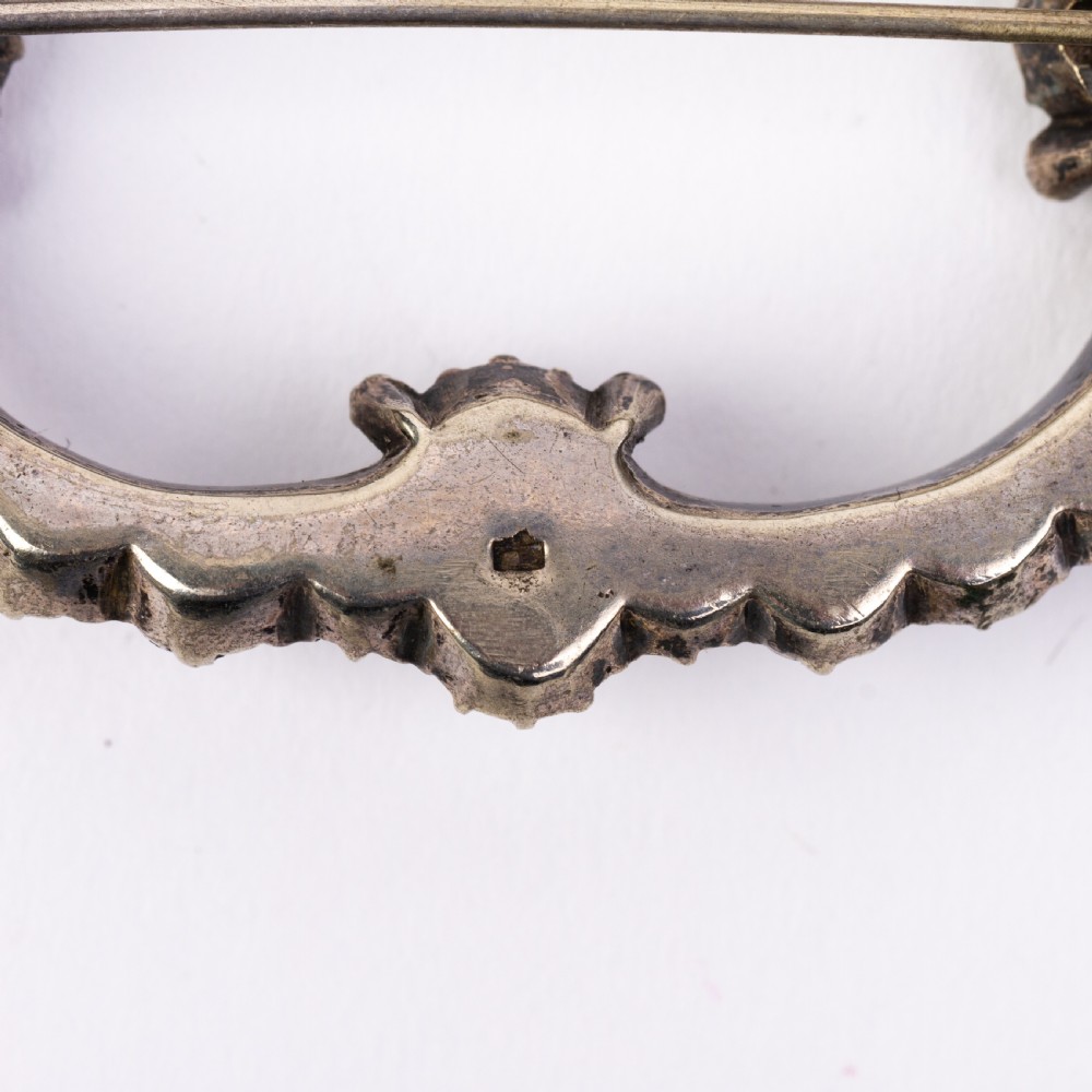 A nineteenth-century Victorian openwork oval buckle brooch set with faceted clear paste glass stones in a silver setting. View VI