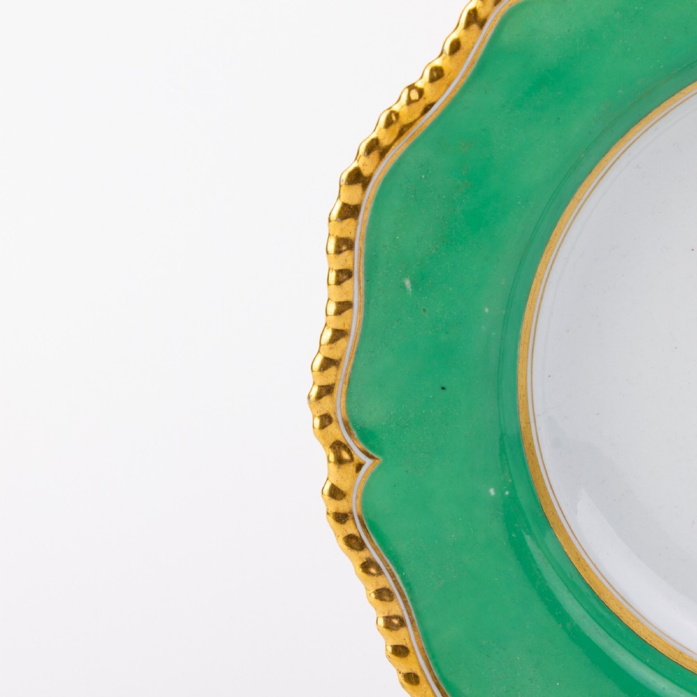 A Regency period Flight Barr and Barr porcelain plate featuring a green border, a gadrooned gilt rim, and a central hand-painted crest with three swords and a serpent. View V