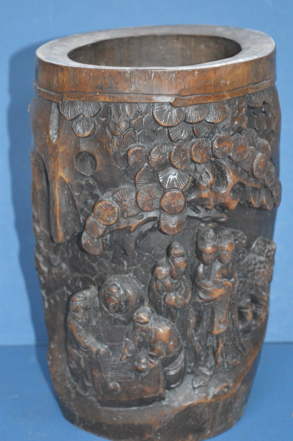 A late nineteenth-century hand-carved dark brown Chinese bamboo brush pot depicting figures and pine trees in high relief.