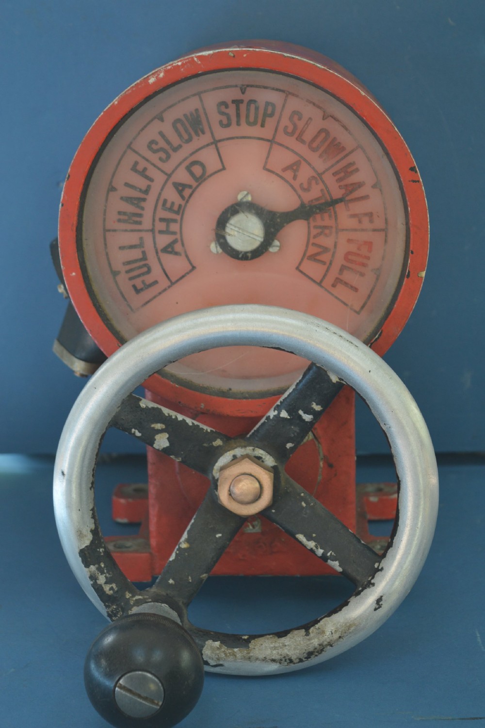 A mid-20th-century red and black painted metal ship engine order telegraph featuring a circular dial with ahead and astern markings behind glass and a four-spoke control wheel.