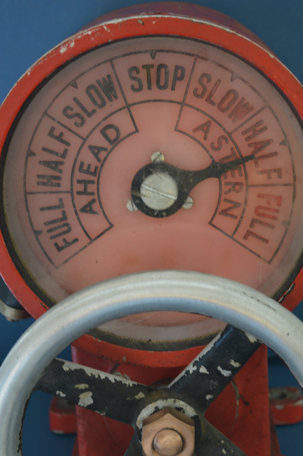 A mid-20th-century red and black painted metal ship engine order telegraph featuring a circular dial with ahead and astern markings behind glass and a four-spoke control wheel. View II