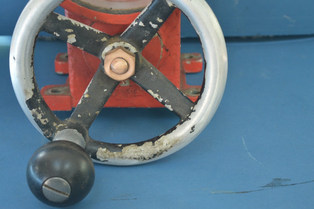 A mid-20th-century red and black painted metal ship engine order telegraph featuring a circular dial with ahead and astern markings behind glass and a four-spoke control wheel. View III