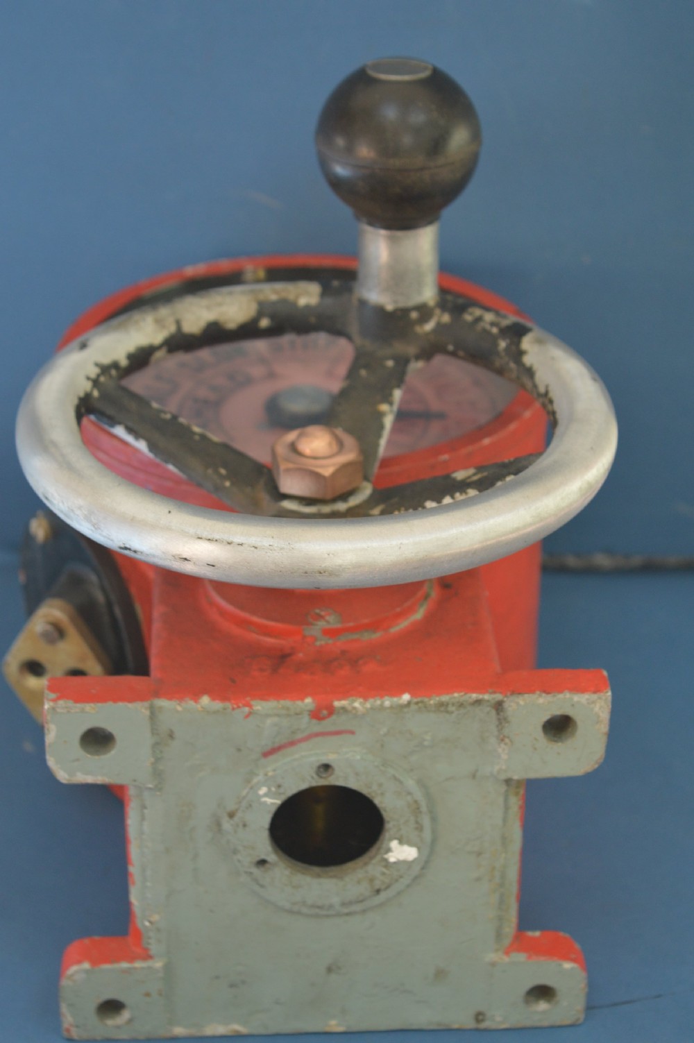 A mid-20th-century red and black painted metal ship engine order telegraph featuring a circular dial with ahead and astern markings behind glass and a four-spoke control wheel. View IX