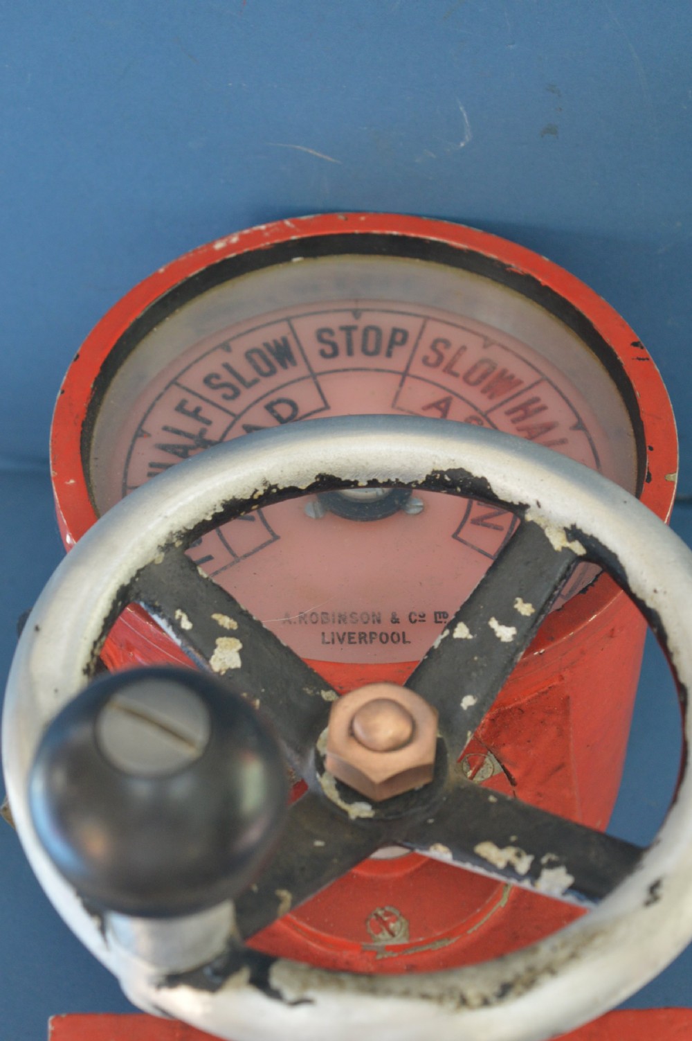 A mid-20th-century red and black painted metal ship engine order telegraph featuring a circular dial with ahead and astern markings behind glass and a four-spoke control wheel. View XII