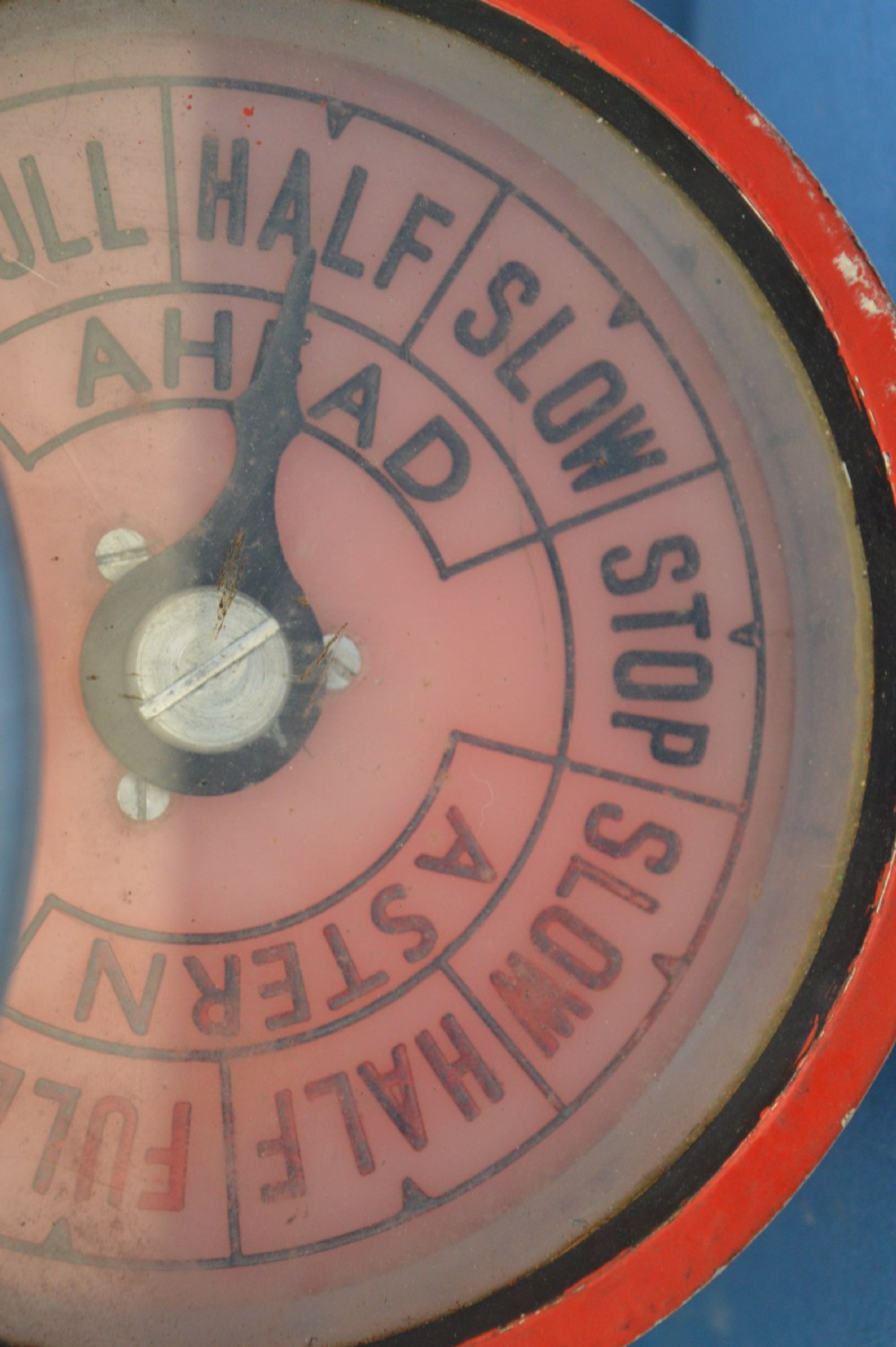 A mid-20th-century red and black painted metal ship engine order telegraph featuring a circular dial with ahead and astern markings behind glass and a four-spoke control wheel. View XIII