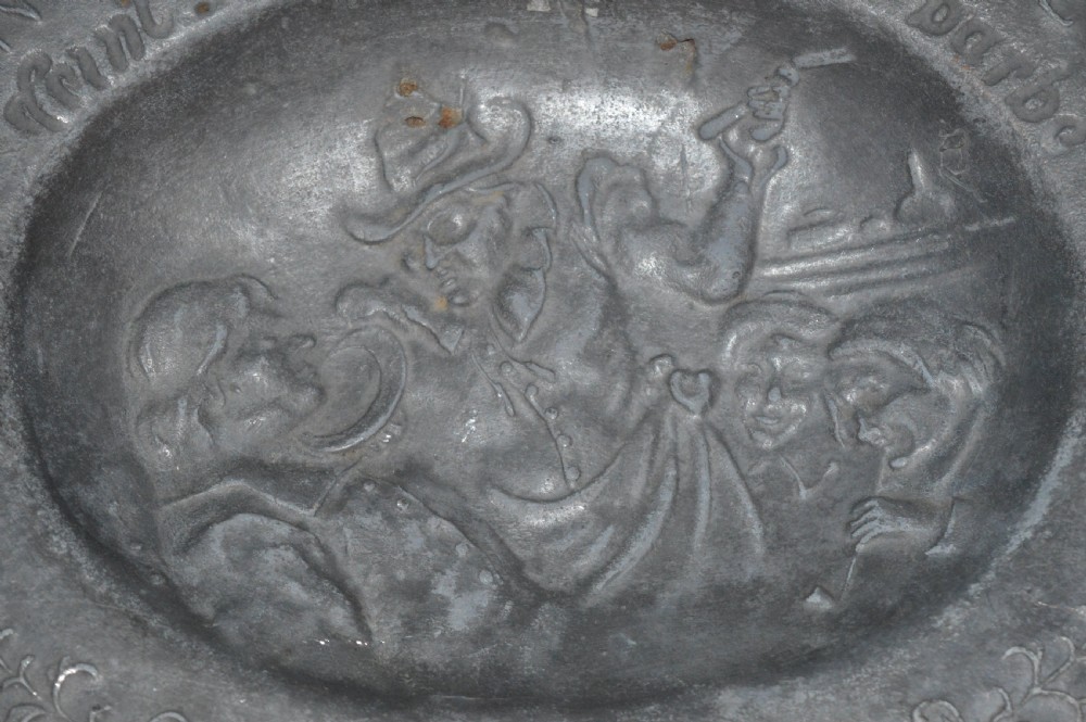 A 19th-century French pewter oval barber bowl with a crescent neck cut-out, embossed rim lettering, and a central relief scene. View IV