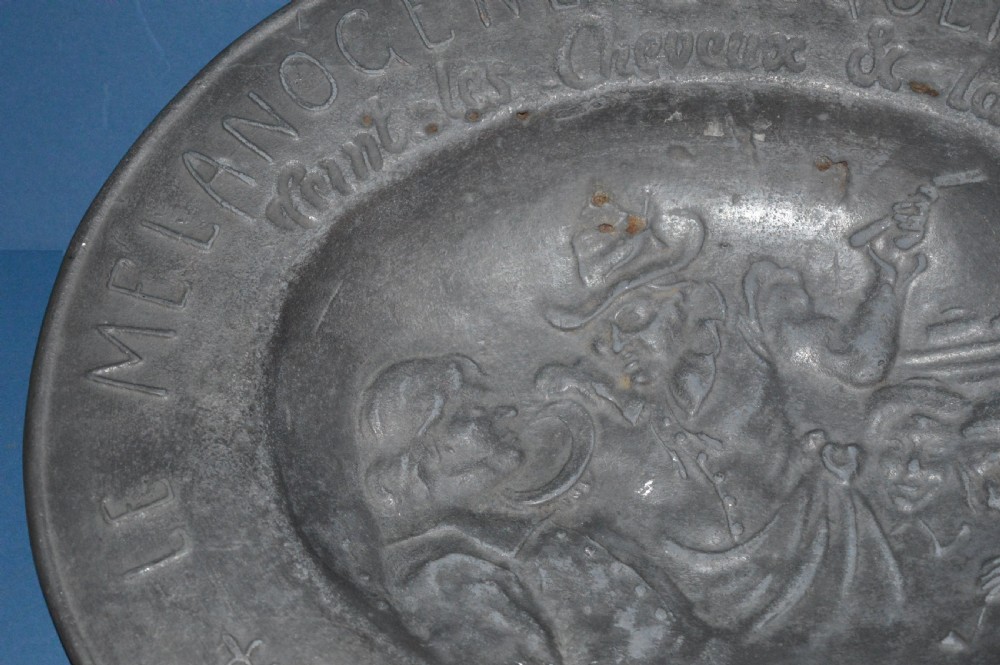 A 19th-century French pewter oval barber bowl with a crescent neck cut-out, embossed rim lettering, and a central relief scene. View V