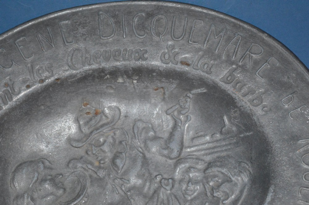 A 19th-century French pewter oval barber bowl with a crescent neck cut-out, embossed rim lettering, and a central relief scene. View VI