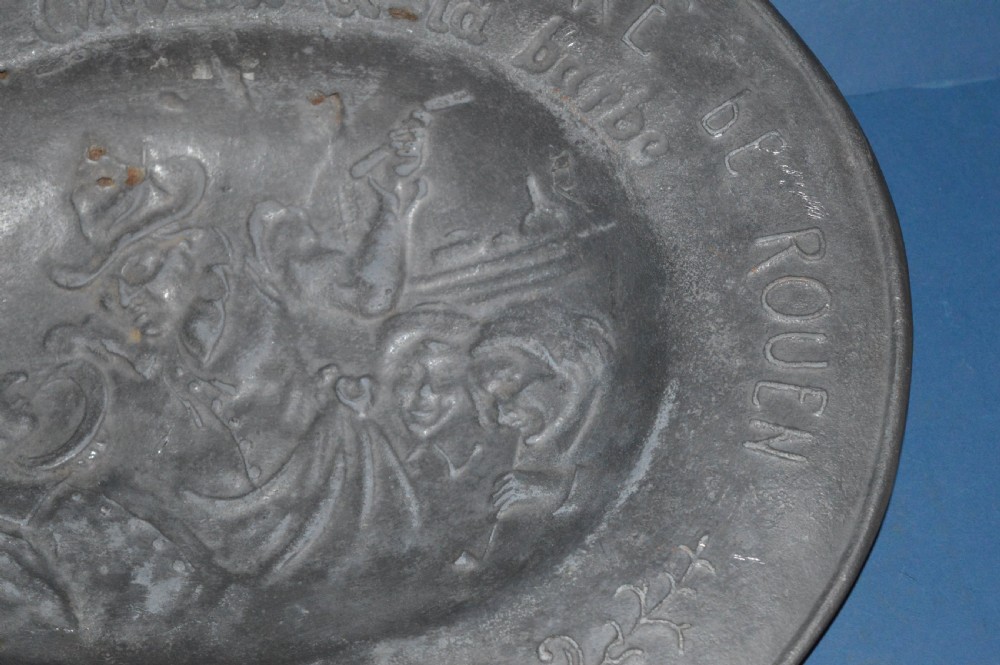 A 19th-century French pewter oval barber bowl with a crescent neck cut-out, embossed rim lettering, and a central relief scene. View VII