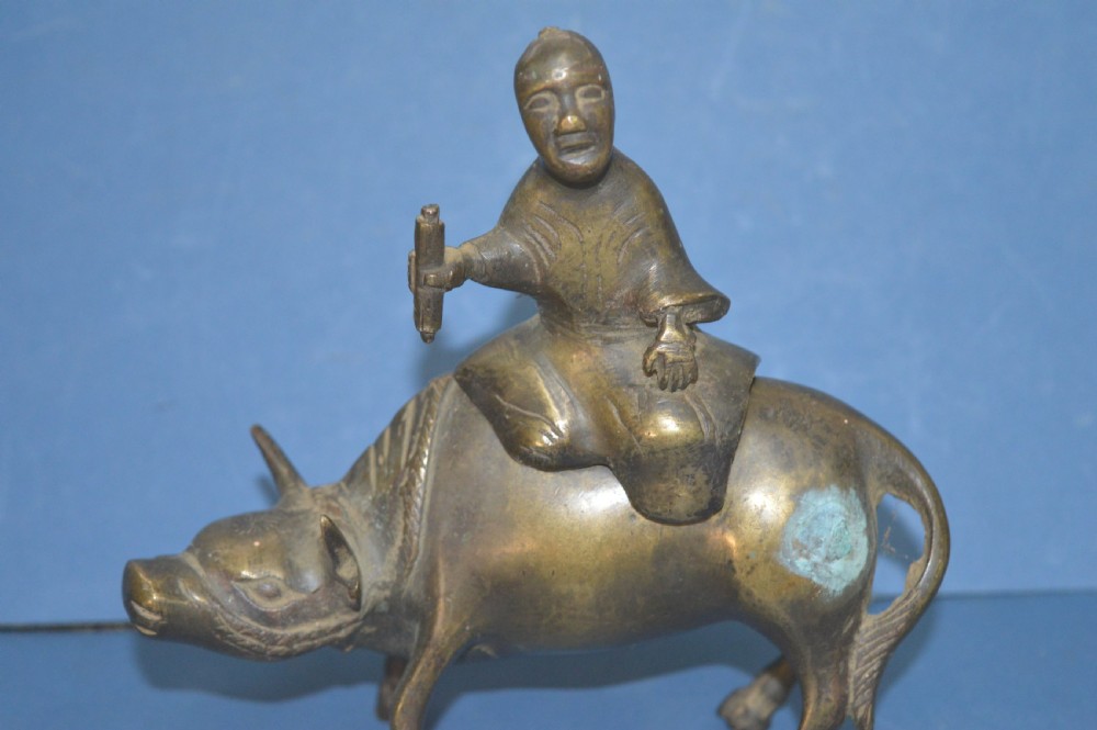 A late 19th-century cast bronze censer depicting a man dressed in robes seated astride a horned ox or water buffalo.