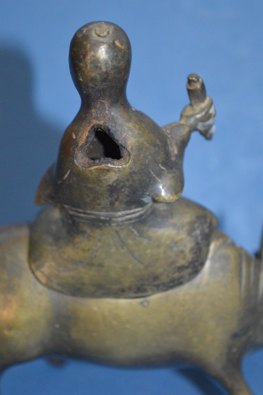 A late 19th-century cast bronze censer depicting a man dressed in robes seated astride a horned ox or water buffalo. View X