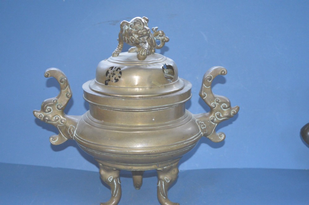 A heavy Chinese bronze lidded censer featuring a foo dog lid finial, pierced cover, double beast side handles, and three tripod feet.