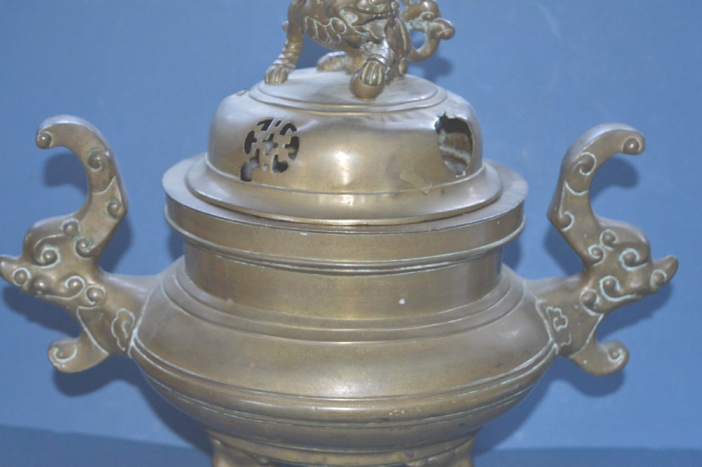 A heavy Chinese bronze lidded censer featuring a foo dog lid finial, pierced cover, double beast side handles, and three tripod feet. View II