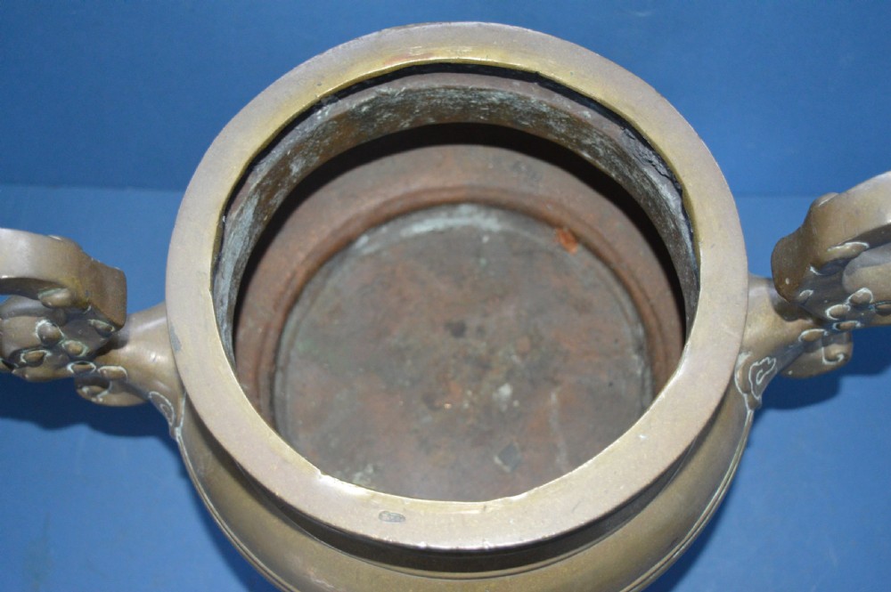 A heavy Chinese bronze lidded censer featuring a foo dog lid finial, pierced cover, double beast side handles, and three tripod feet. View VII