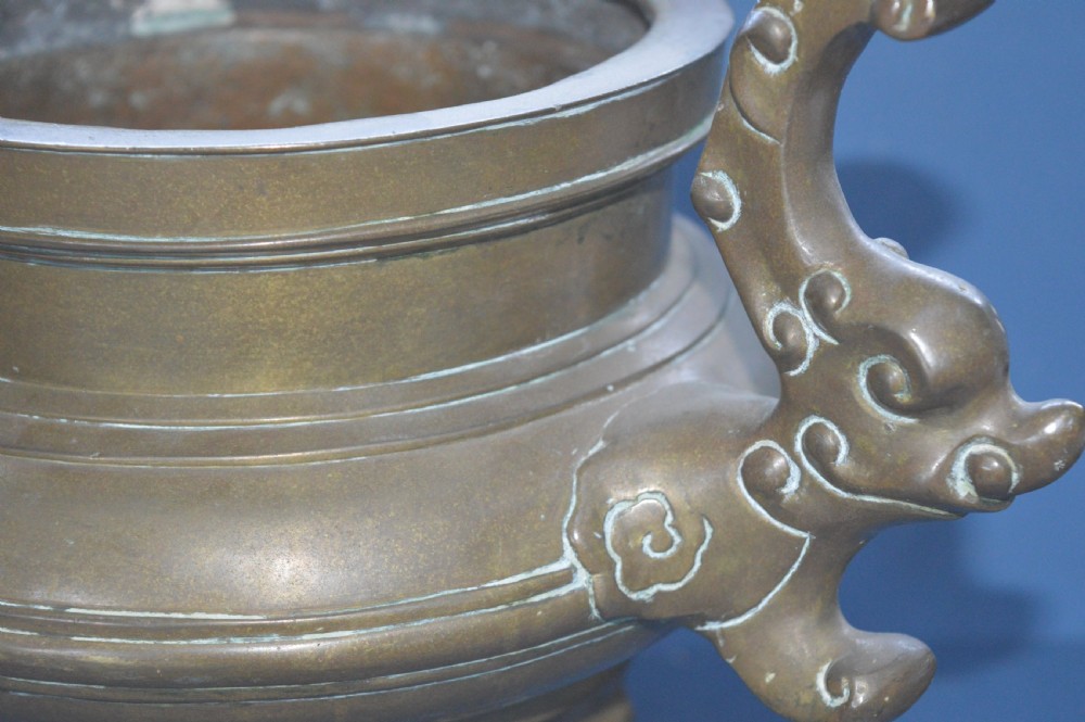 A heavy Chinese bronze lidded censer featuring a foo dog lid finial, pierced cover, double beast side handles, and three tripod feet. View X