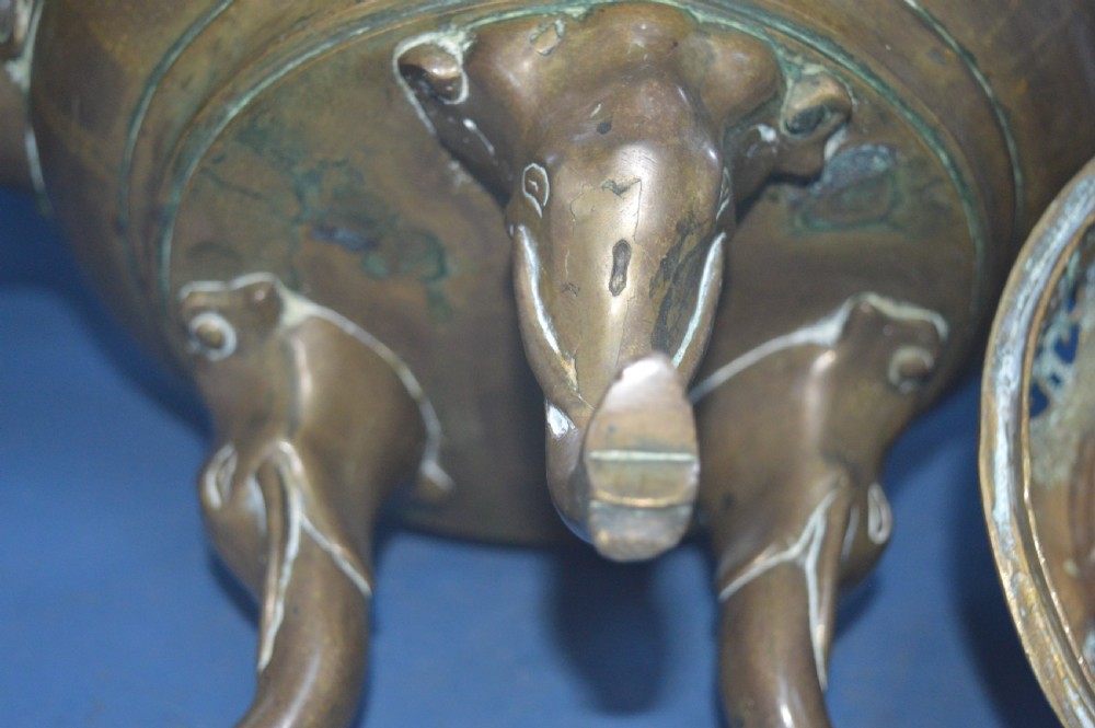 A heavy Chinese bronze lidded censer featuring a foo dog lid finial, pierced cover, double beast side handles, and three tripod feet. View XII