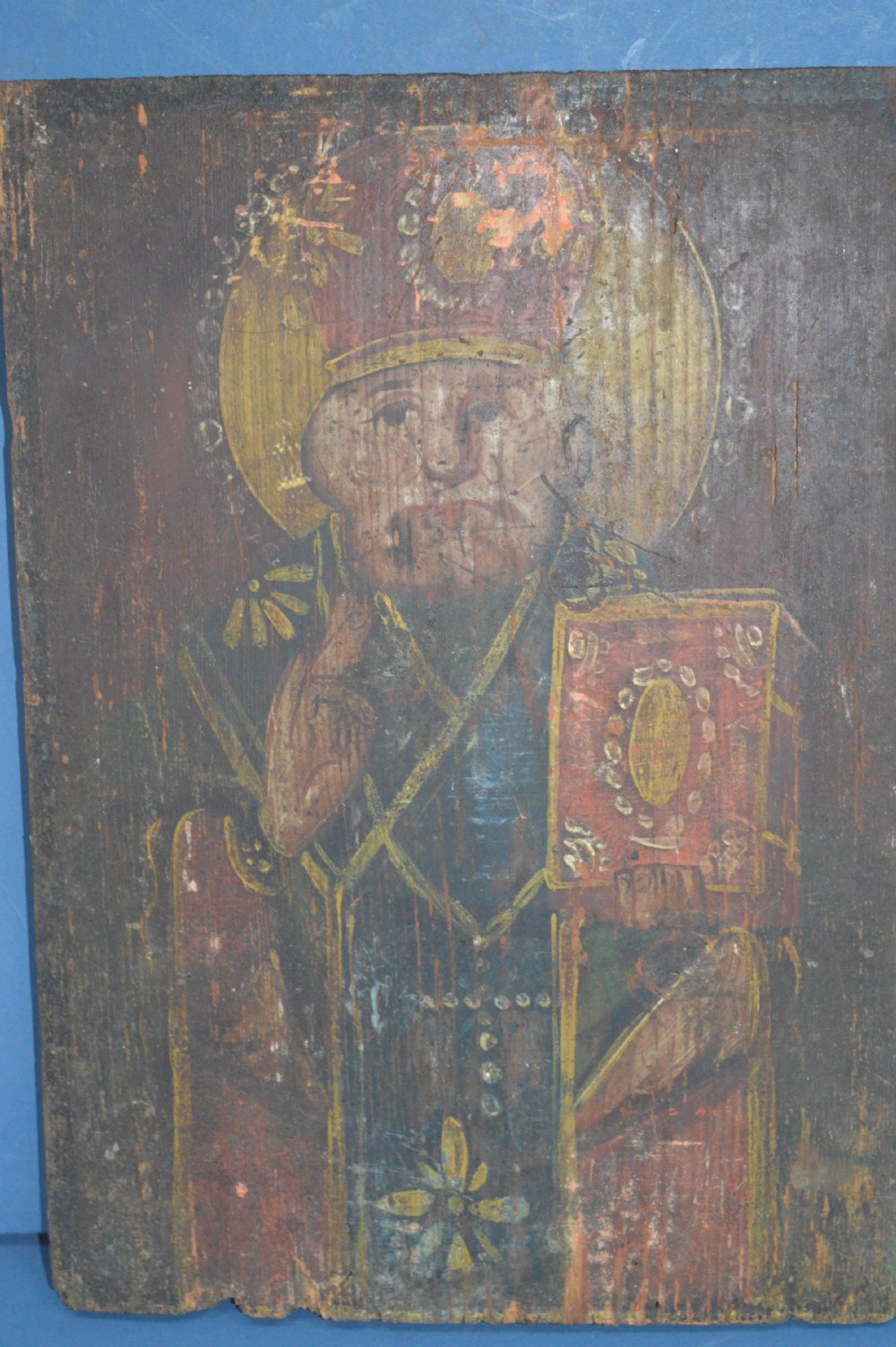 An antique hand-painted Russian wooden icon depicting a religious figure with a halo and holding a scripture book.