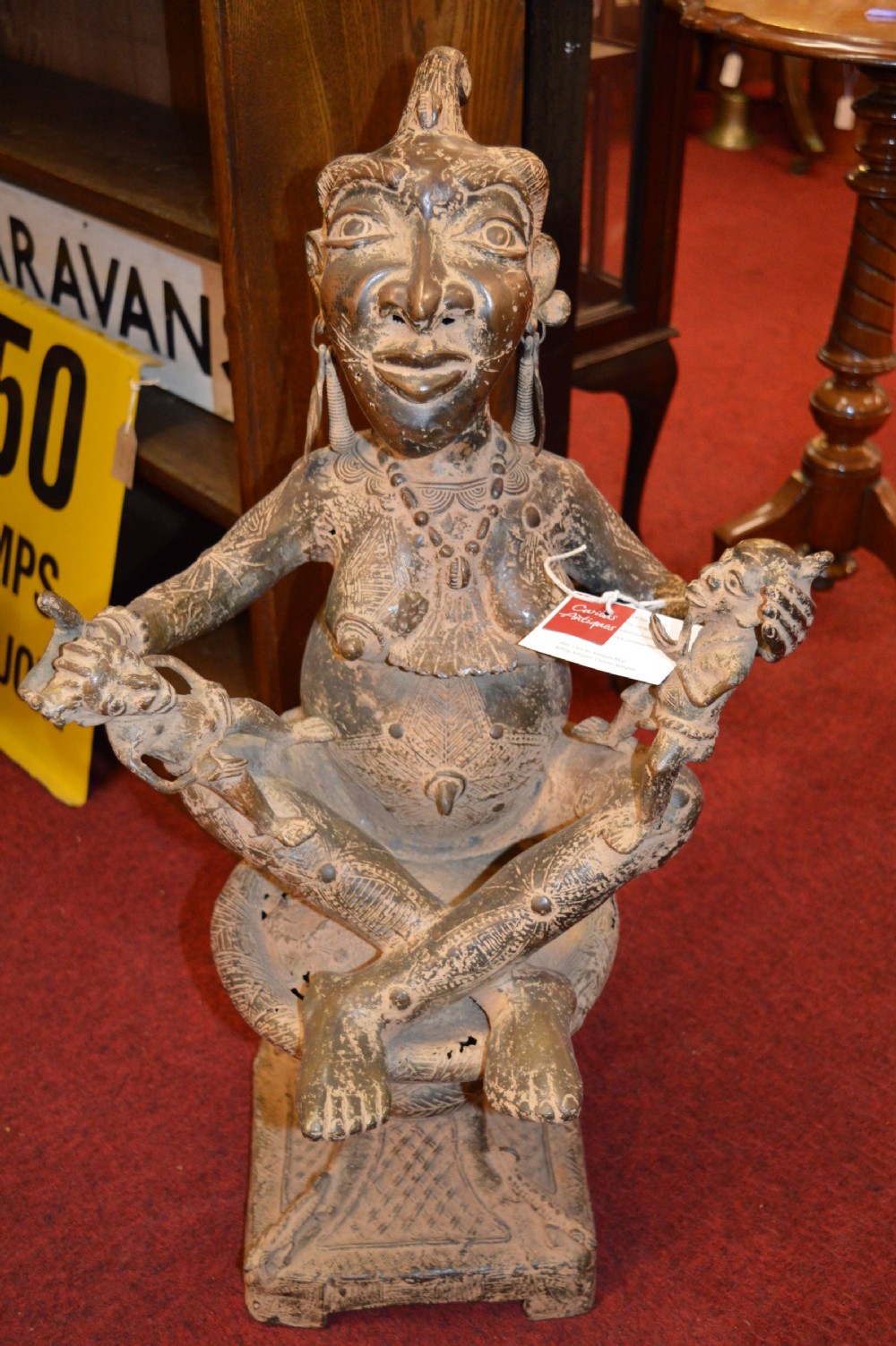 A cast bronze West African maternity statue depicting a seated female figure with elaborate headwear and detailed surface carving holding two smaller child figures.