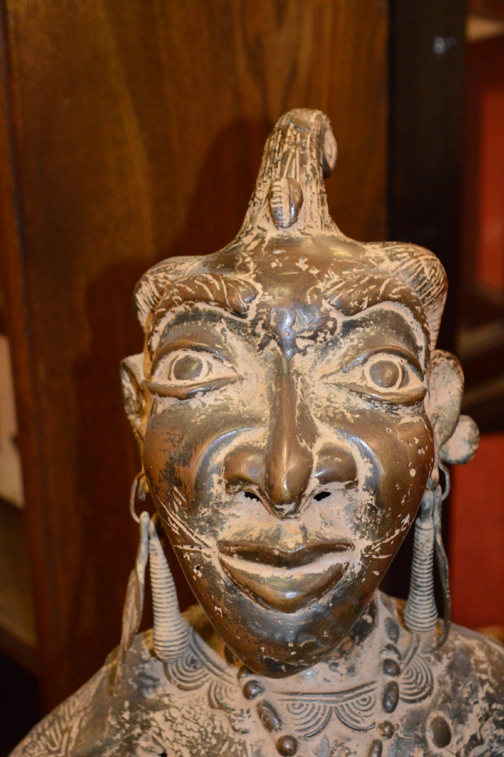 A cast bronze West African maternity statue depicting a seated female figure with elaborate headwear and detailed surface carving holding two smaller child figures. View II
