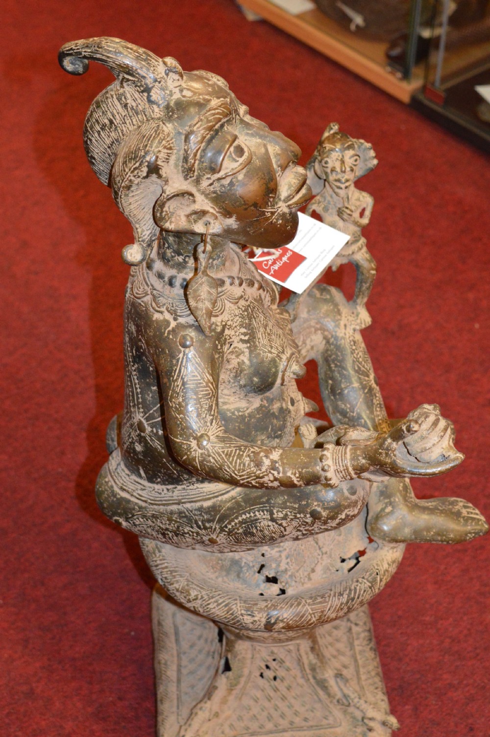 A cast bronze West African maternity statue depicting a seated female figure with elaborate headwear and detailed surface carving holding two smaller child figures. View VI