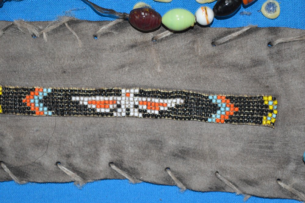 A framed display case lined with blue cloth containing Native American artefacts, including a beaded leather pouch, trade beads, arrowheads, and a hafted tool. View VI