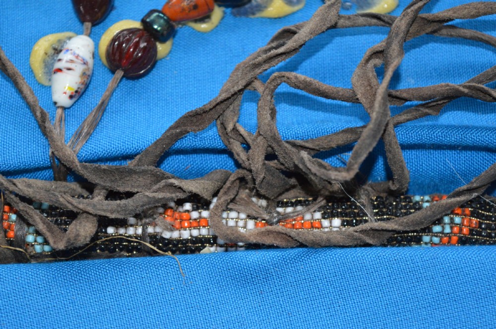 A framed display case lined with blue cloth containing Native American artefacts, including a beaded leather pouch, trade beads, arrowheads, and a hafted tool. View XVI