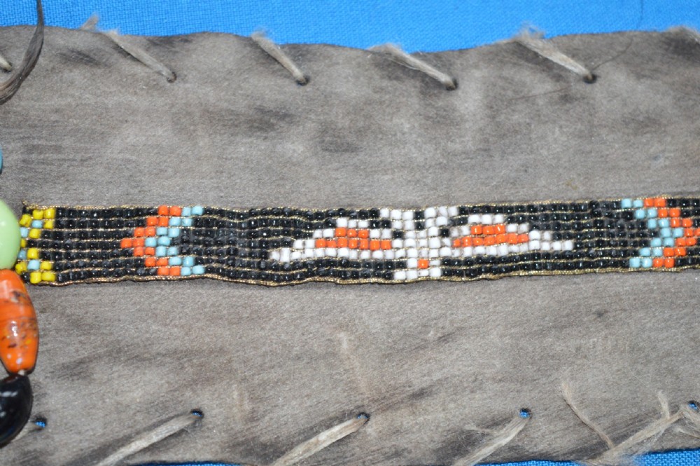 A framed display case lined with blue cloth containing Native American artefacts, including a beaded leather pouch, trade beads, arrowheads, and a hafted tool. View XVII
