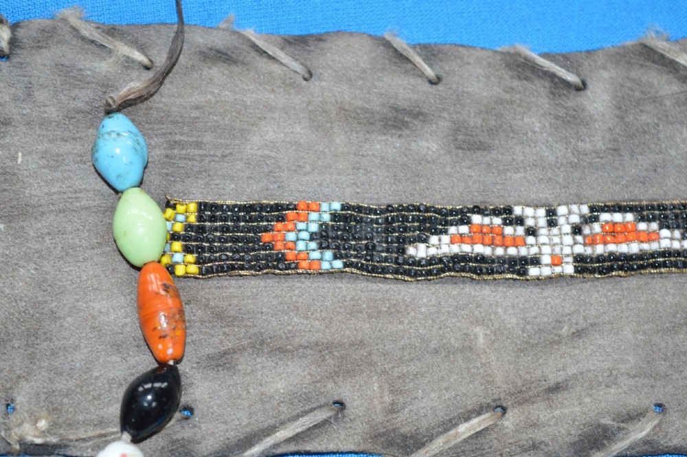 A framed display case lined with blue cloth containing Native American artefacts, including a beaded leather pouch, trade beads, arrowheads, and a hafted tool. View XVIII
