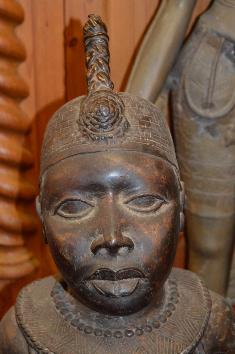 A standing cast bronze West African warrior figure with ceremonial headwear, detailed chest ornamentation, and traditional waist garment. View III