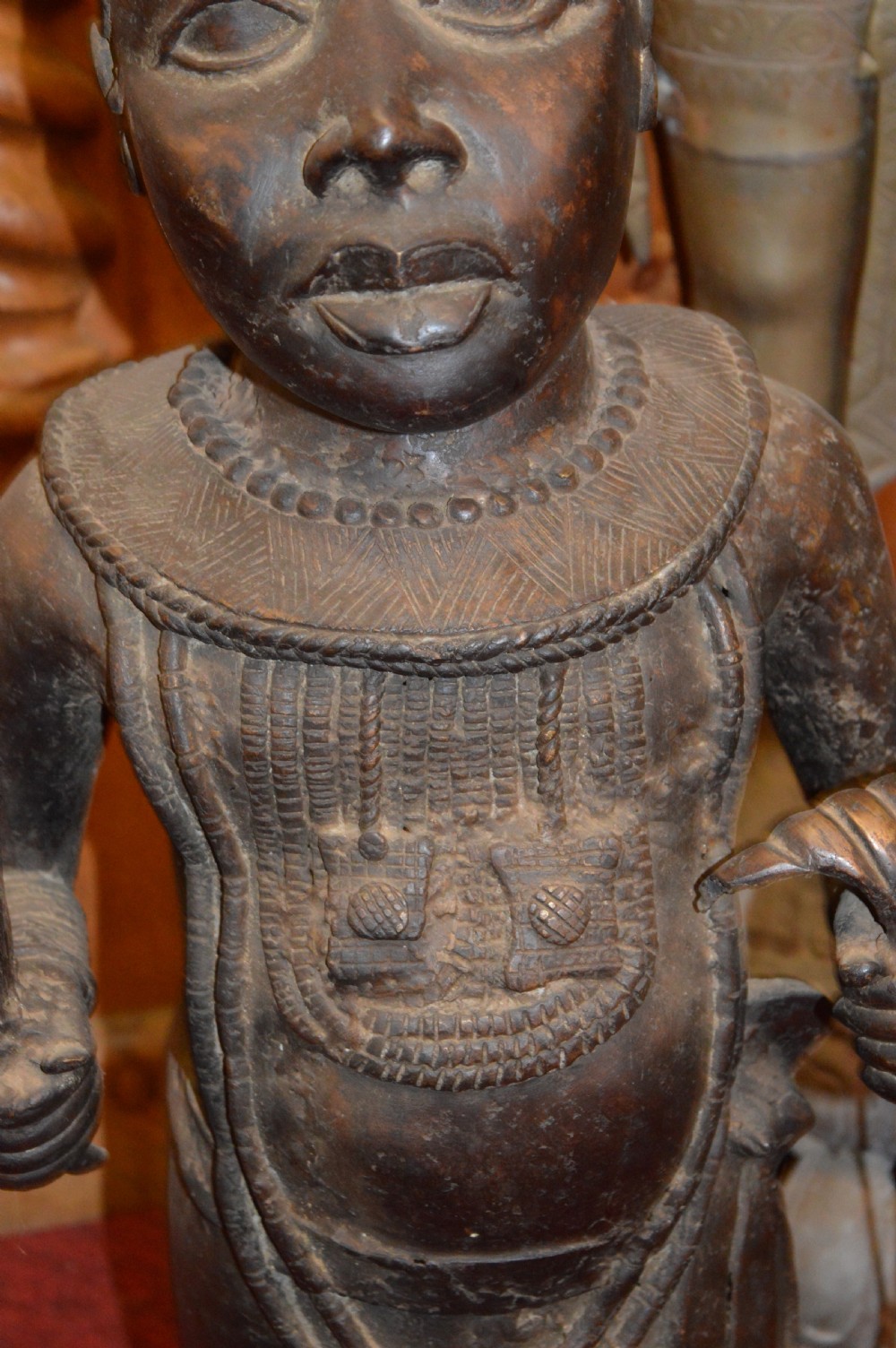 A standing cast bronze West African warrior figure with ceremonial headwear, detailed chest ornamentation, and traditional waist garment. View IV
