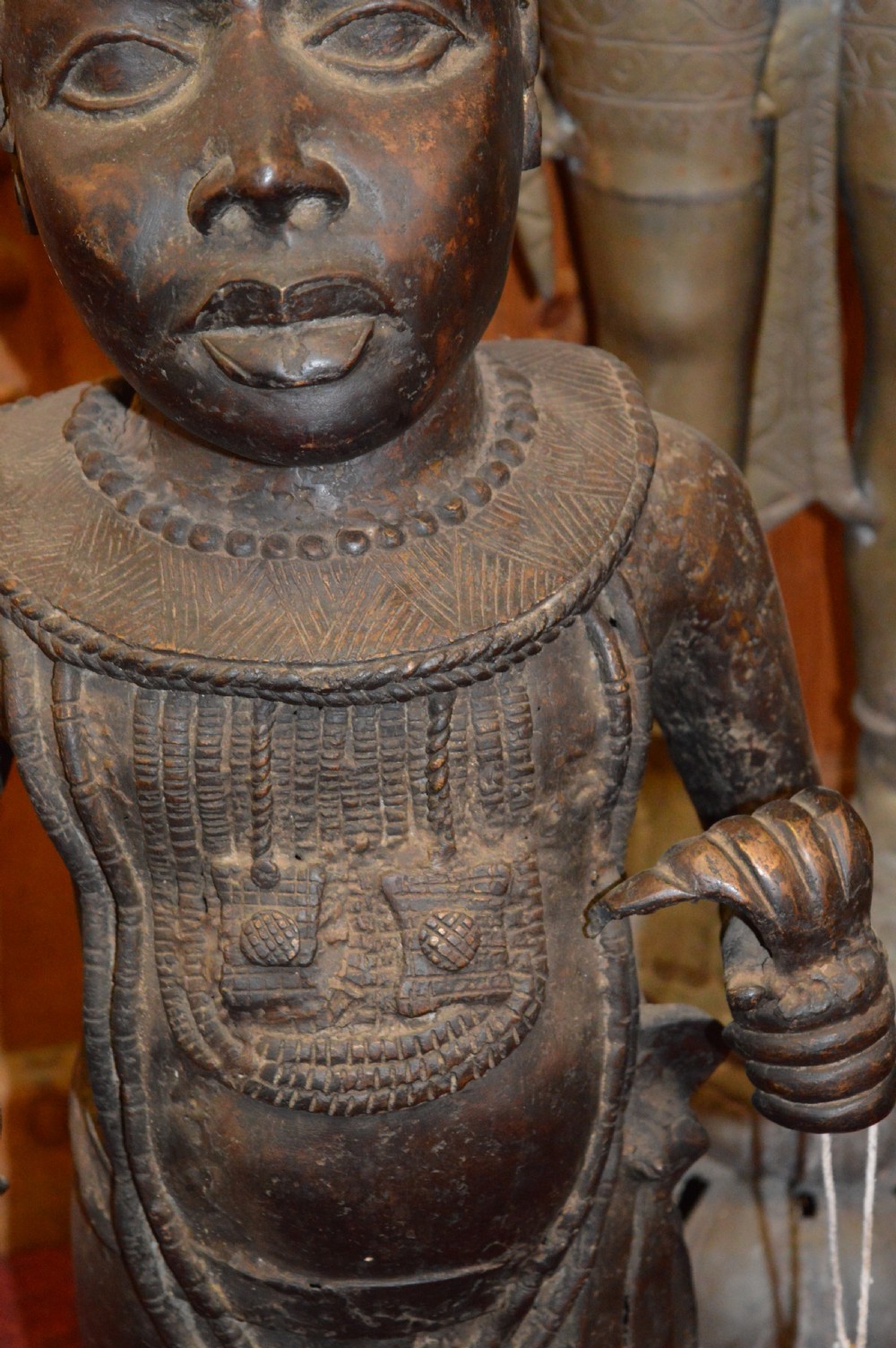 A standing cast bronze West African warrior figure with ceremonial headwear, detailed chest ornamentation, and traditional waist garment. View V
