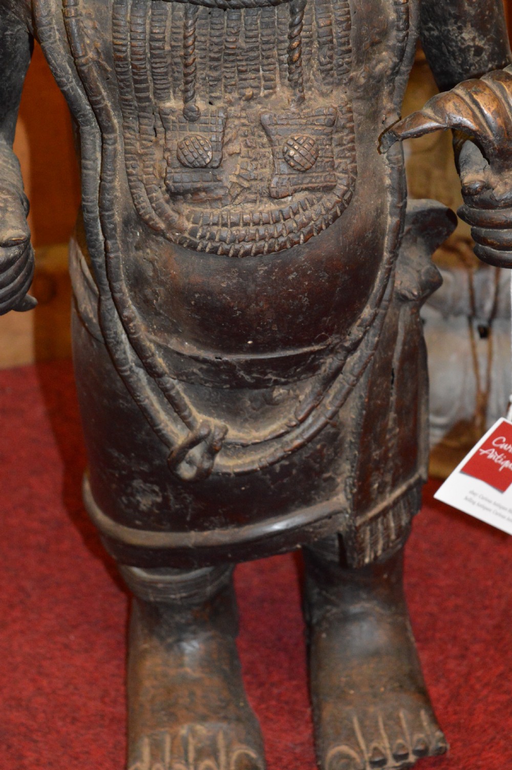 A standing cast bronze West African warrior figure with ceremonial headwear, detailed chest ornamentation, and traditional waist garment. View VII