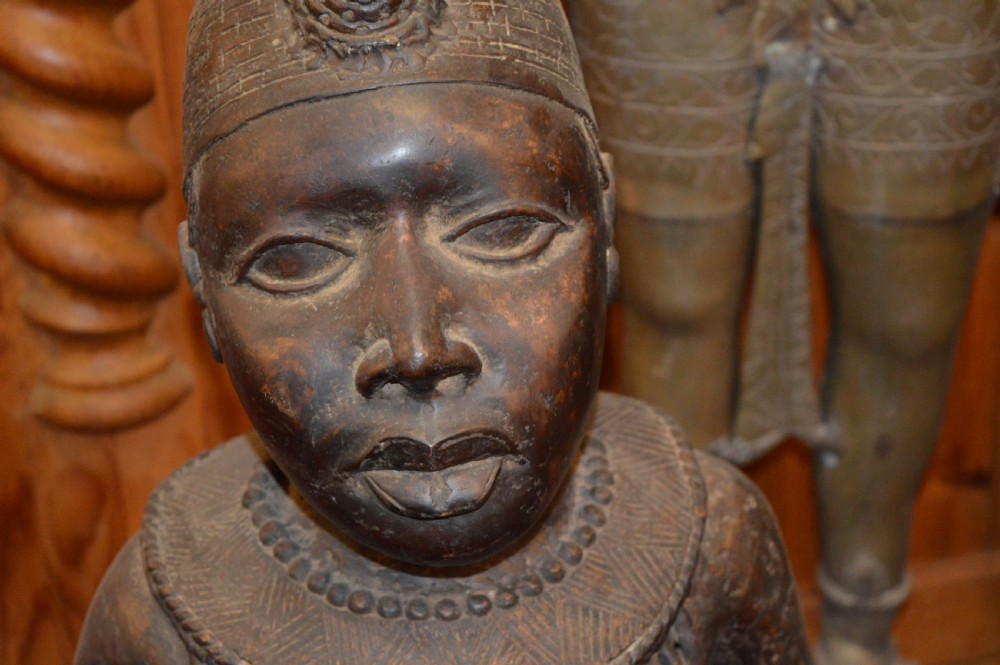 A standing cast bronze West African warrior figure with ceremonial headwear, detailed chest ornamentation, and traditional waist garment. View IX