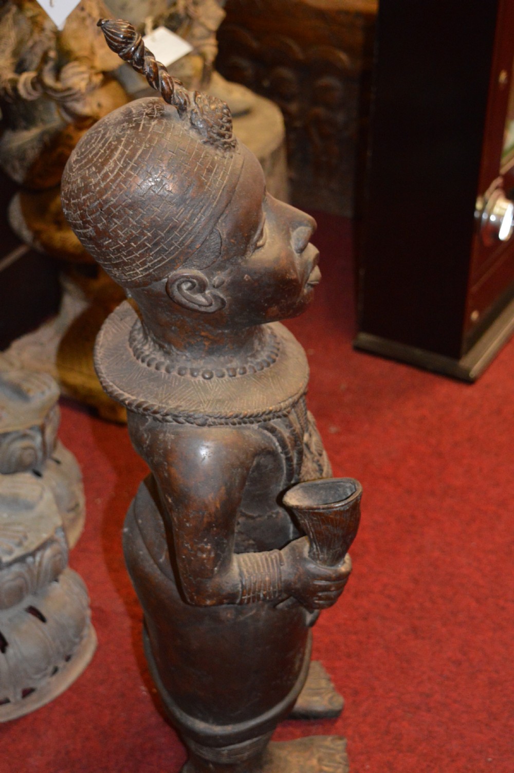 A standing cast bronze West African warrior figure with ceremonial headwear, detailed chest ornamentation, and traditional waist garment. View XI