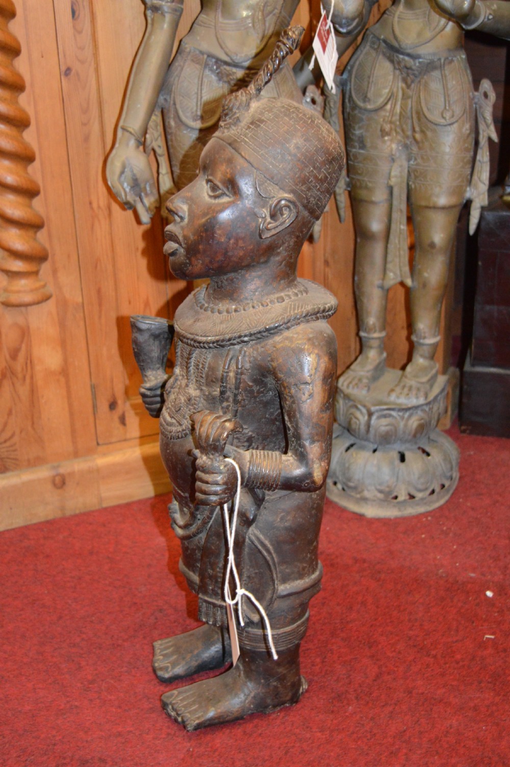 A standing cast bronze West African warrior figure with ceremonial headwear, detailed chest ornamentation, and traditional waist garment. View XII