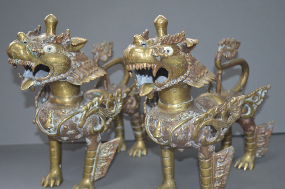 A pair of 19th-century cast bronze Tibetan temple lions featuring stylized wings, open jaws, and original patinated surface.