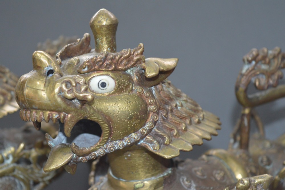 A pair of 19th-century cast bronze Tibetan temple lions featuring stylized wings, open jaws, and original patinated surface. View II