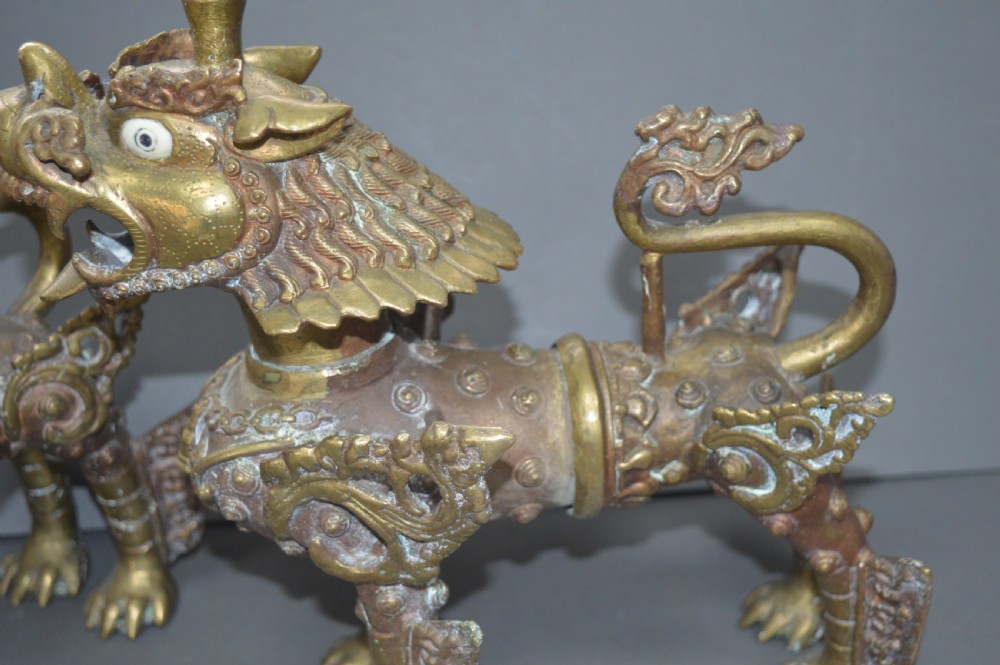 A pair of 19th-century cast bronze Tibetan temple lions featuring stylized wings, open jaws, and original patinated surface. View V