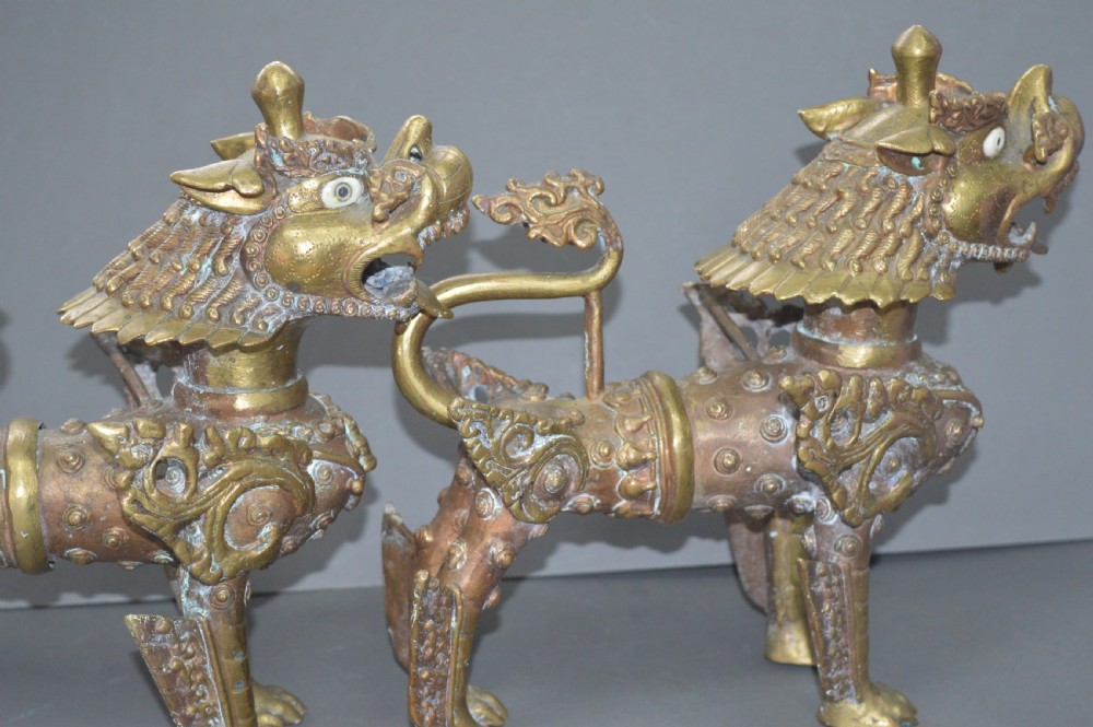 A pair of 19th-century cast bronze Tibetan temple lions featuring stylized wings, open jaws, and original patinated surface. View X