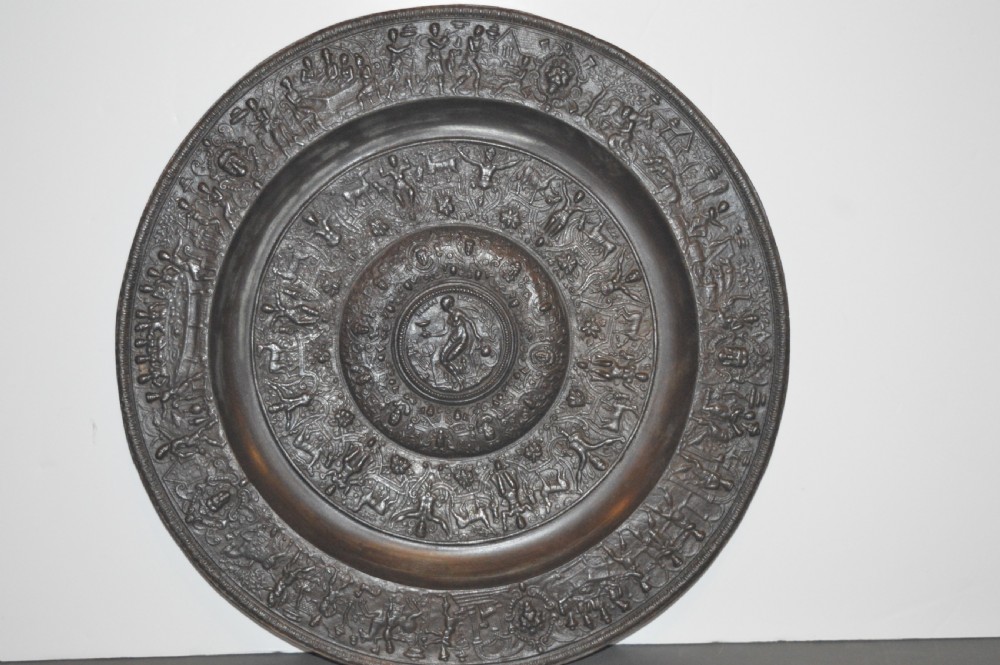 A large circular dark bronze charger featuring concentric bands of classical relief figures surrounding a central classical medallion.