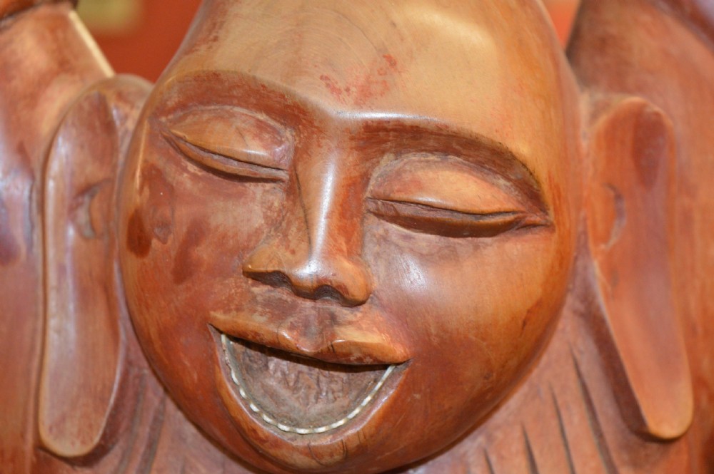 A nineteenth-century carved wooden statue depicting a laughing Buddha figure standing with arms raised above its head. View VI