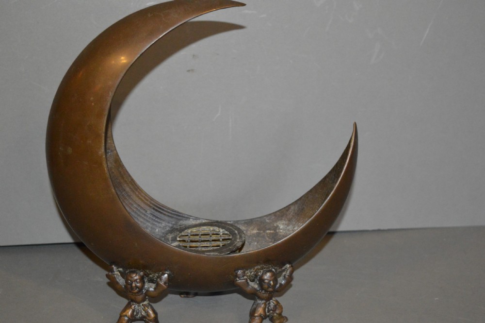 A bronze incense burner crafted in a crescent moon shape with figural supports and a central removable grate.