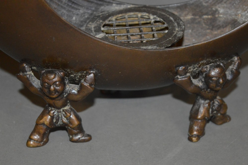 A bronze incense burner crafted in a crescent moon shape with figural supports and a central removable grate. View II