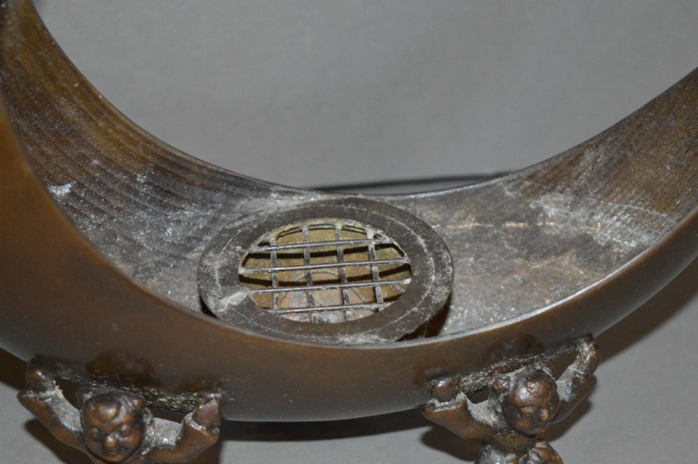 A bronze incense burner crafted in a crescent moon shape with figural supports and a central removable grate. View III