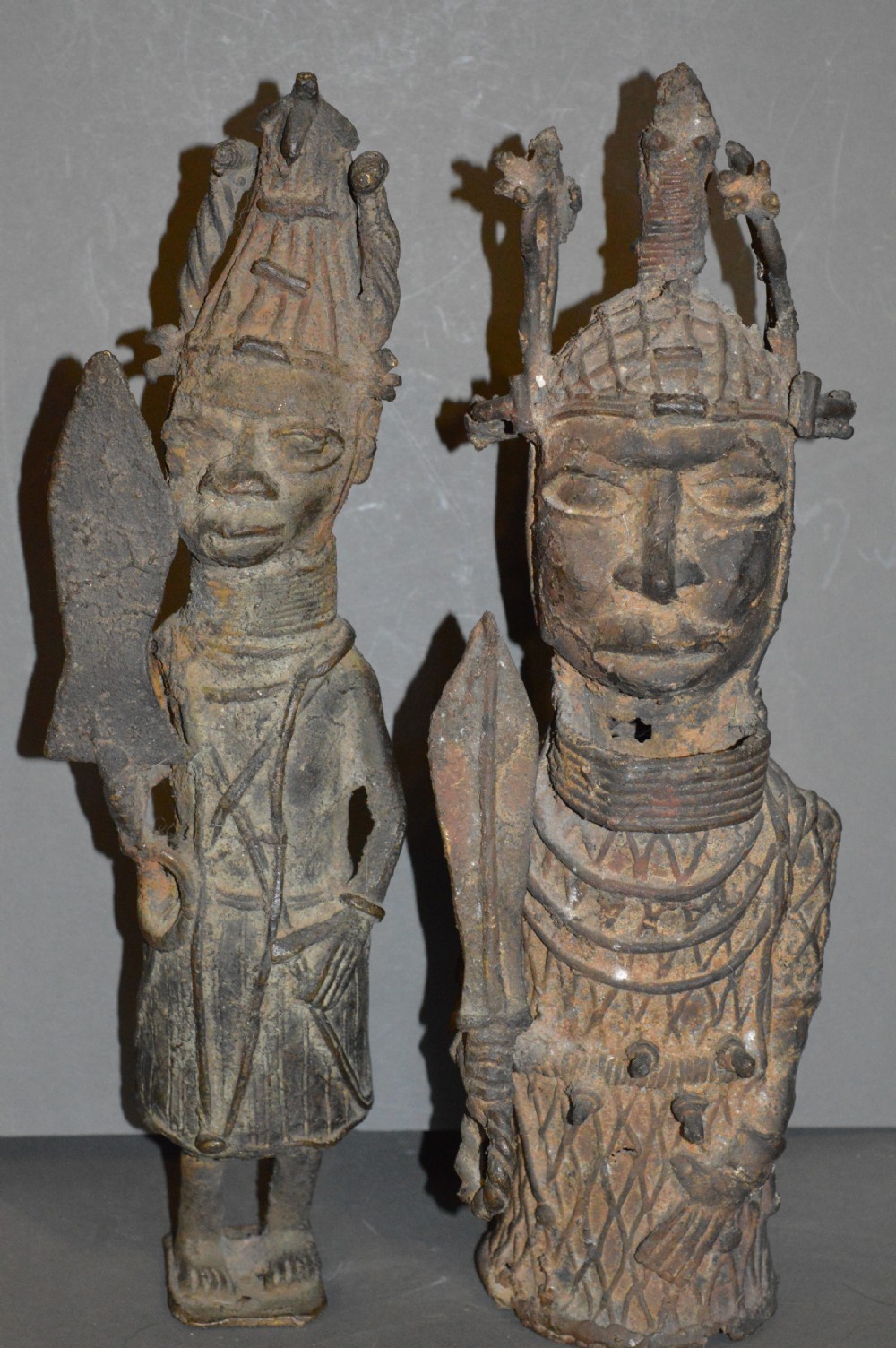A pair of cast bronze West African warrior statues featuring textured headpieces, patterned garments, and held spears.