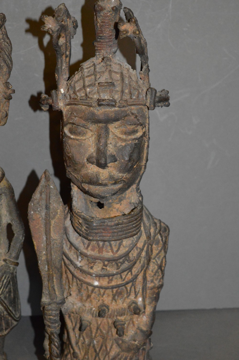 A pair of cast bronze West African warrior statues featuring textured headpieces, patterned garments, and held spears. View II