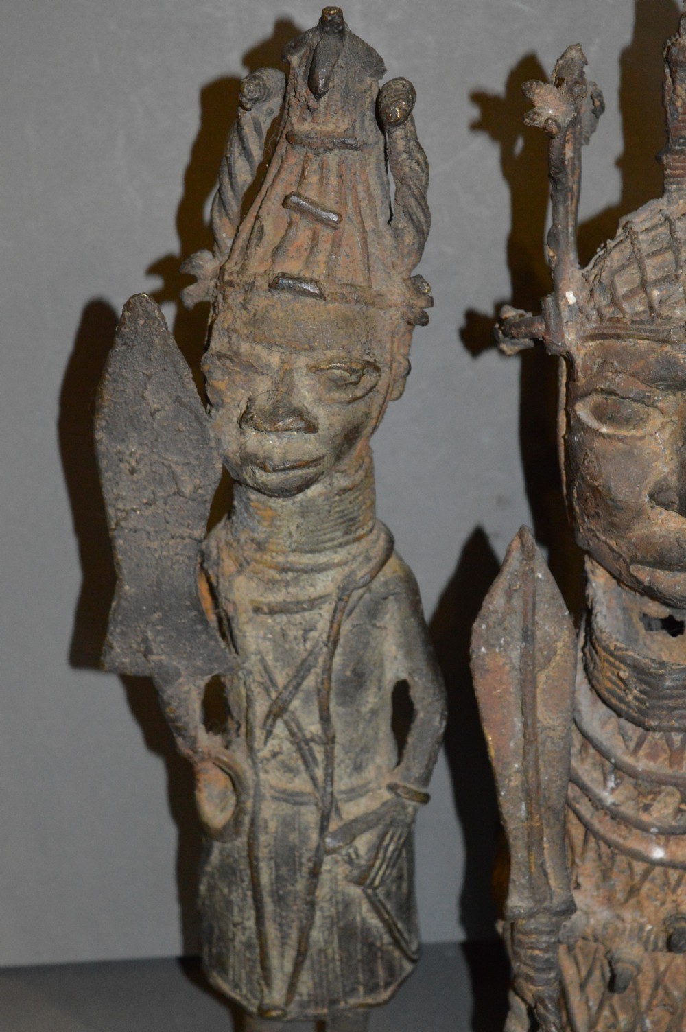 A pair of cast bronze West African warrior statues featuring textured headpieces, patterned garments, and held spears. View III