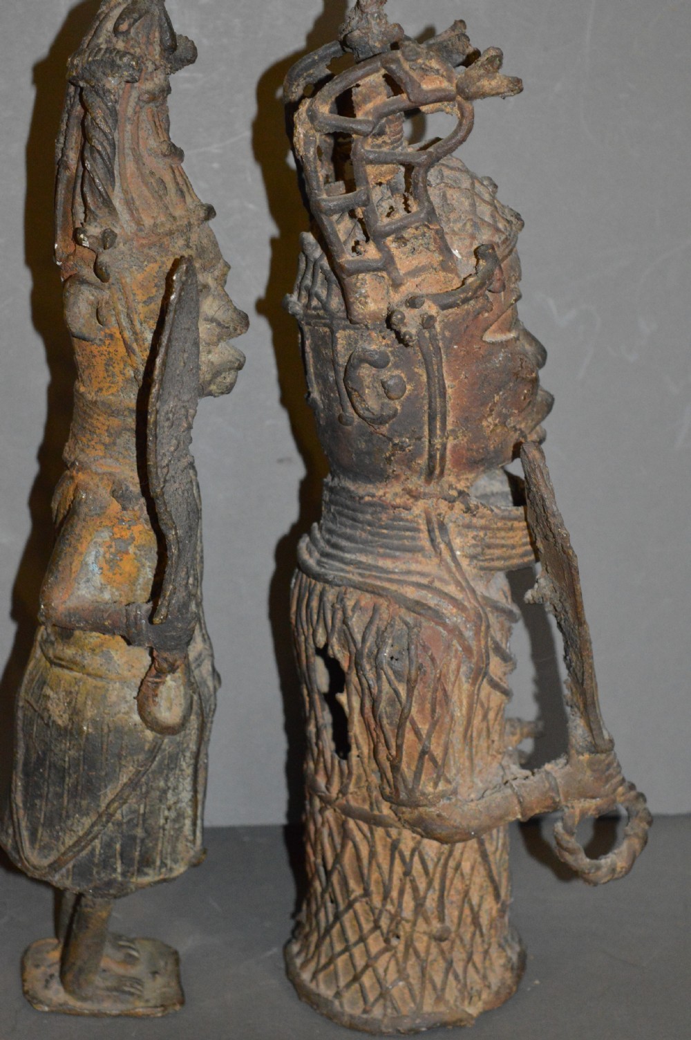 A pair of cast bronze West African warrior statues featuring textured headpieces, patterned garments, and held spears. View V