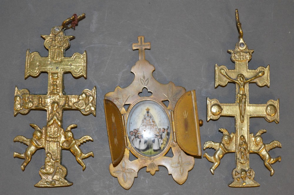 A set of three late nineteenth-century Spanish brass devotional items, including two Caravaca double-barred crosses with angel figures and one central hinged miniature shrine.